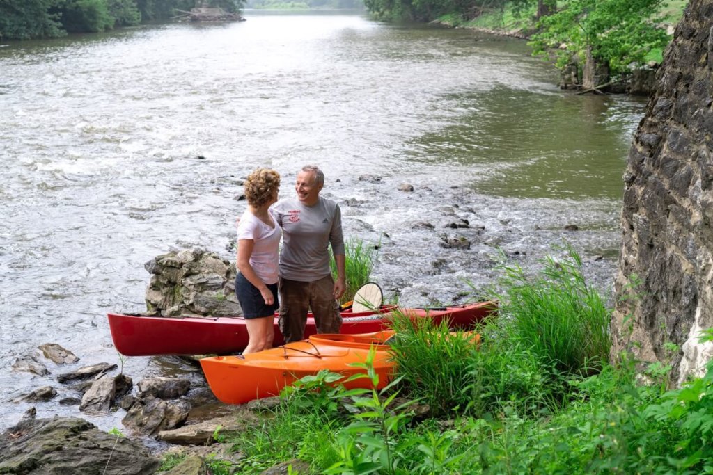 older man and woman standing with kayaks creekside